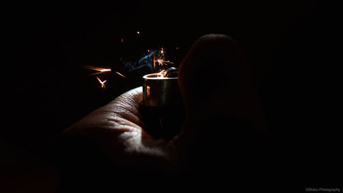 Close-up of hand holding lit candle in darkroom