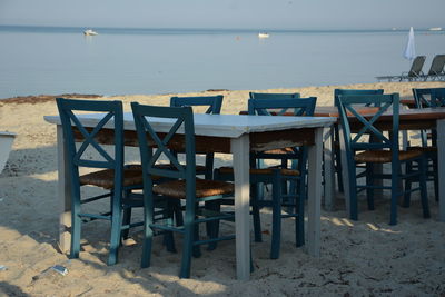 Chairs and table on beach by sea against sky
