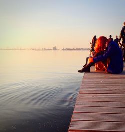 People on pier over river during sunset