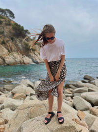 Full length of young woman standing on rock at sea shore