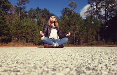 Woman doing yoga while sitting on road against trees