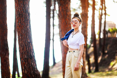 Portrait of woman standing against tree trunk in forest