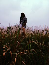 Low angle view of young woman standing on grassy field against sky