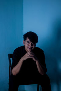 Portrait of young man sitting against blue wall