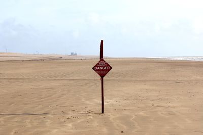 Road sign on beach against sky