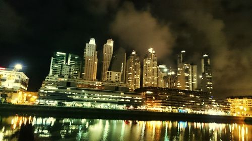 Illuminated city by river against sky at night