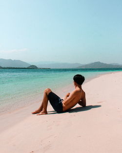 Woman sitting on beach against sky