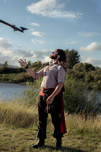 Man standing on field by lake against sky