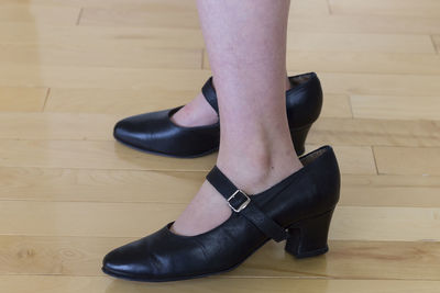 Low section of woman wearing shoes on hardwood floor