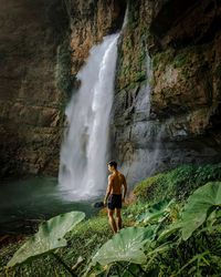 Full length of man standing on rock against waterfall