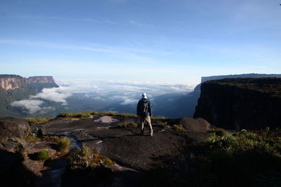 Rear view of man standing on mountain looking at landscape against sky