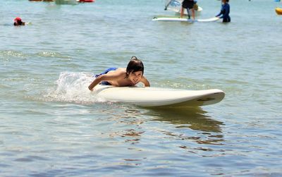 Shirtless boy surfboarding in sea