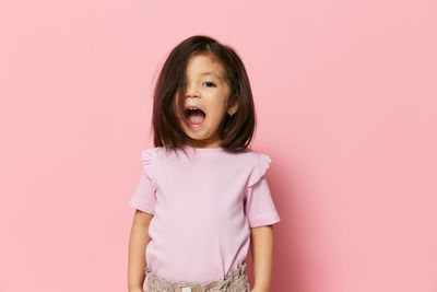 Portrait of young woman standing against pink background