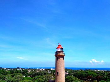 Lighthouse amidst buildings and sea against blue sky