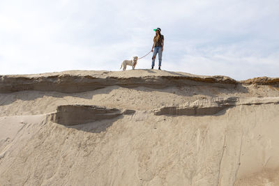 Young woman walking with her dog on the sand in desert