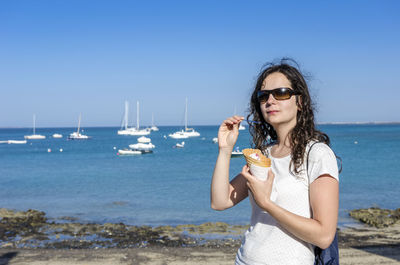 Portrait of beautiful woman standing on beach against clear sky