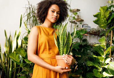 Portrait of teenage girl holding potted plant amid plants