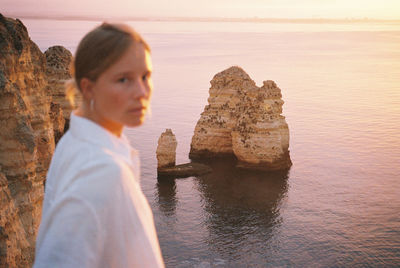 Woman looking at rock formation in sea against sky