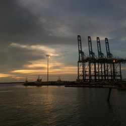 Cranes at pier against sky during sunset