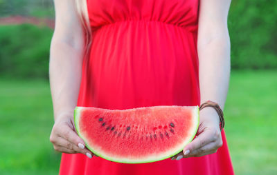 Midsection of pregnant woman holding slice of watermelon
