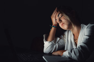 Young woman using mobile phone while sitting against black background