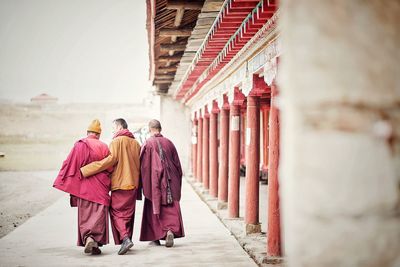 Rear view of monks walking on walkway by temple