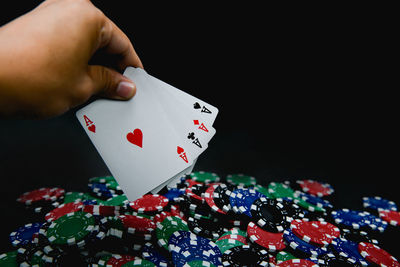 Cropped hand holding playing cards over gambling chips against black background