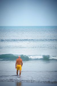 Full length of shirtless man on beach against clear sky