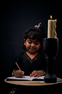 Close-up of girl looking at table against black background