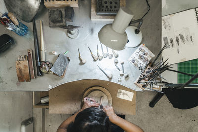 High angle view of female artisan making jewelry on wooden table in workshop