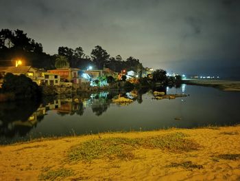 Scenic view of lake by illuminated buildings against sky at night