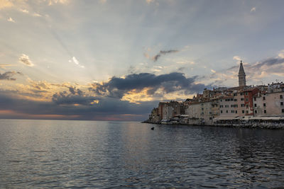 Sea by buildings against sky during sunset