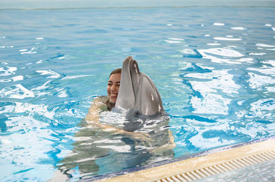 Smiling young woman with dolphin swimming in pool