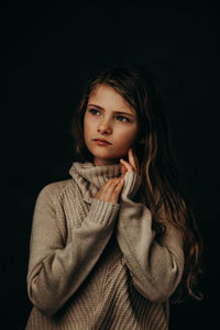 Portrait of beautiful young woman standing against black background