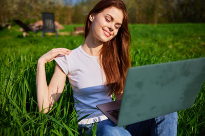 Young woman using laptop while sitting on field