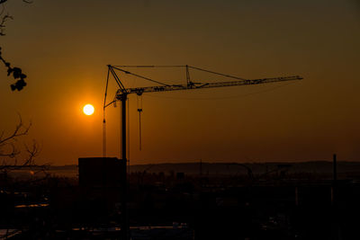 Silhouette cranes at construction site against sky during sunset