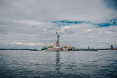 Statue of liberty by sea against cloudy sky