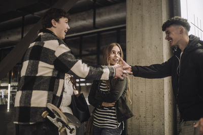 Side view of smiling boy doing handshake with male teenage friend at mall