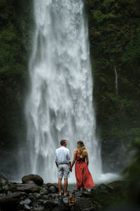 Rear view of people looking at waterfall in forest
