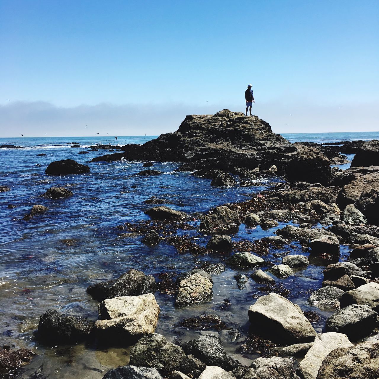 MAN STANDING ON ROCK AGAINST SEA