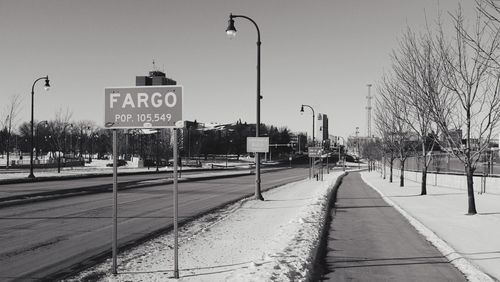 Sign board on snow covered field by street against sky