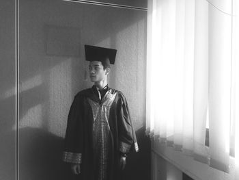 Young man in graduation gown standing at home