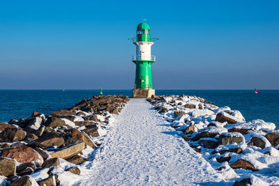 Lighthouse by sea against blue sky