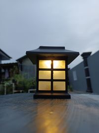 Illuminated lamp on table by building against sky at dusk