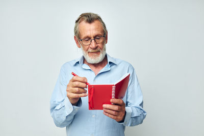 Senior man writing in diary against white background