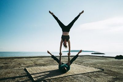 Full length of man balancing woman on hand by sea against clear sky