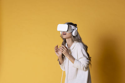 Portrait of young woman using mobile phone while standing against yellow background