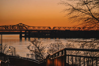 Silhouette bridge over river against sky during sunset