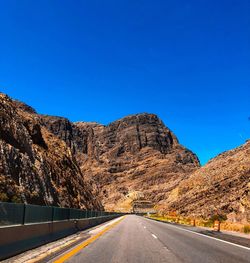 Road amidst mountains against clear blue sky