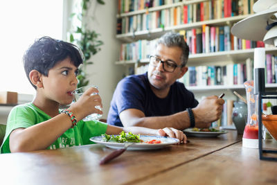 Father looking at son drinking water during lunch